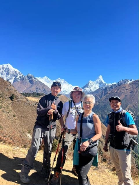David with three fellow trekkers giving a thumbs up on a dry ridge, Ama Dablam and snowy peaks behind under a clear blue sky