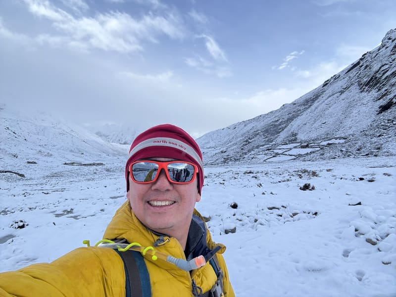 David in a yellow jacket and red beanie grinning in a snow-covered valley